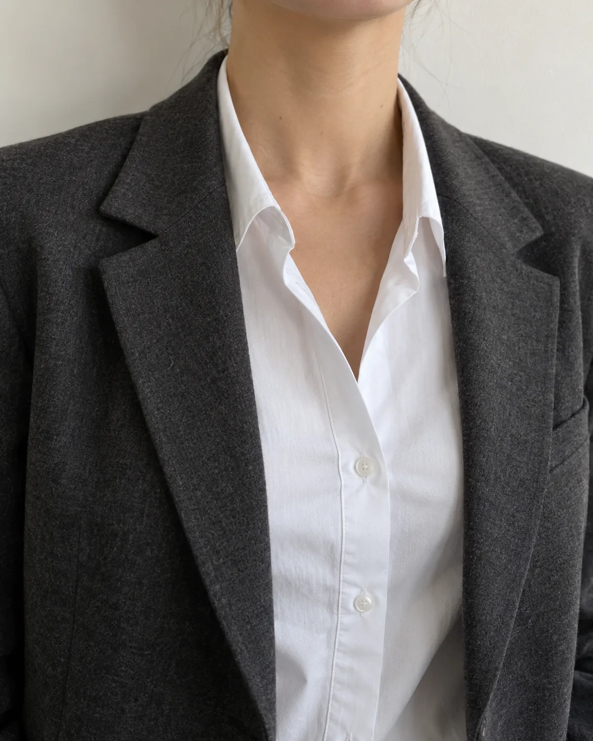 Close crop on the shoulder and lapel area of a charcoal soft-shoulder wool blazer worn over a white stretch cotton button-front shirt with the collar lying flat