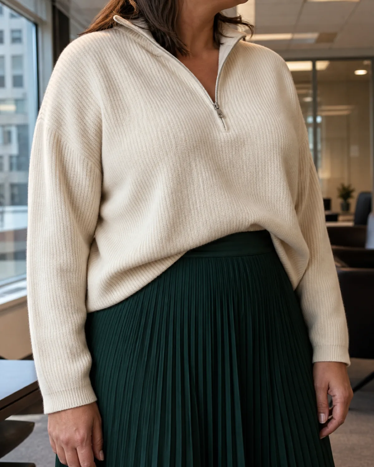 Close crop on a cream half-zip sweater half-tucked into a forest green pleated midi skirt showing the tuck and waistband