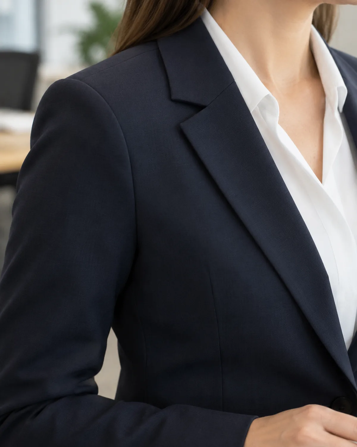 Close crop on the shoulder and collar area of a woman wearing a dark navy blazer over a white blouse with the shoulder seam sitting exactly on the shoulder point and the lapel lying flat and crisp