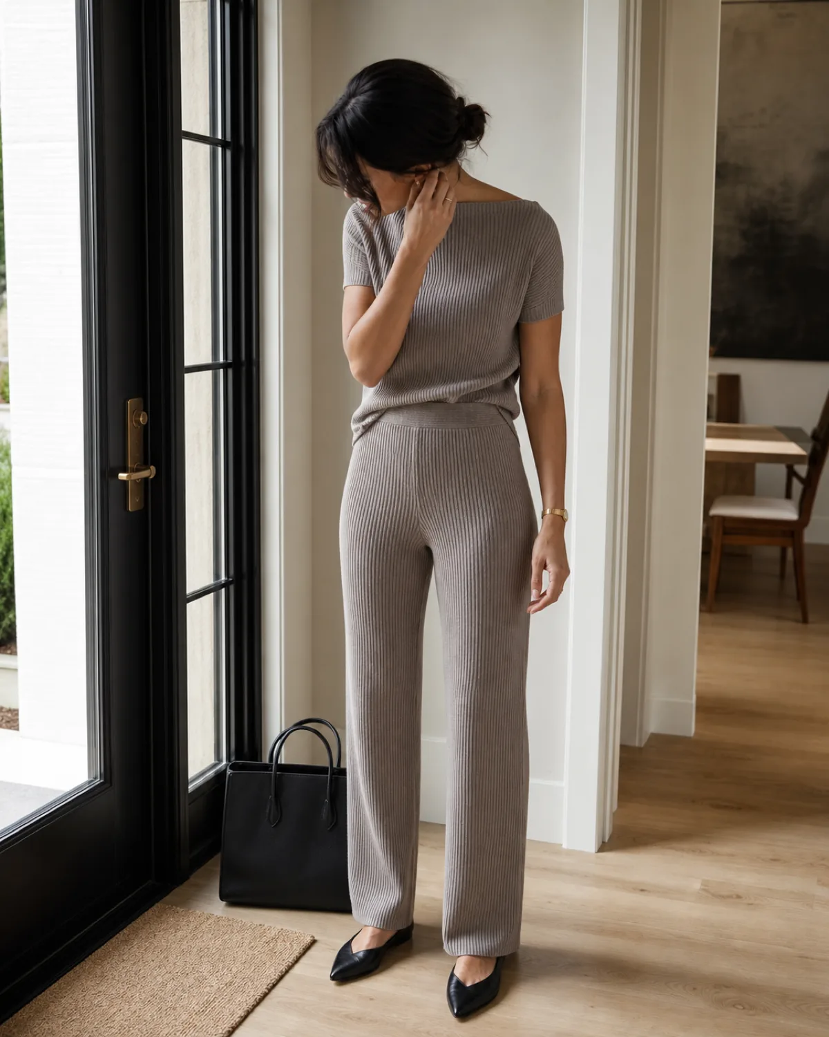 A woman in a taupe ribbed knit co-ord set standing in a home entryway, looking down