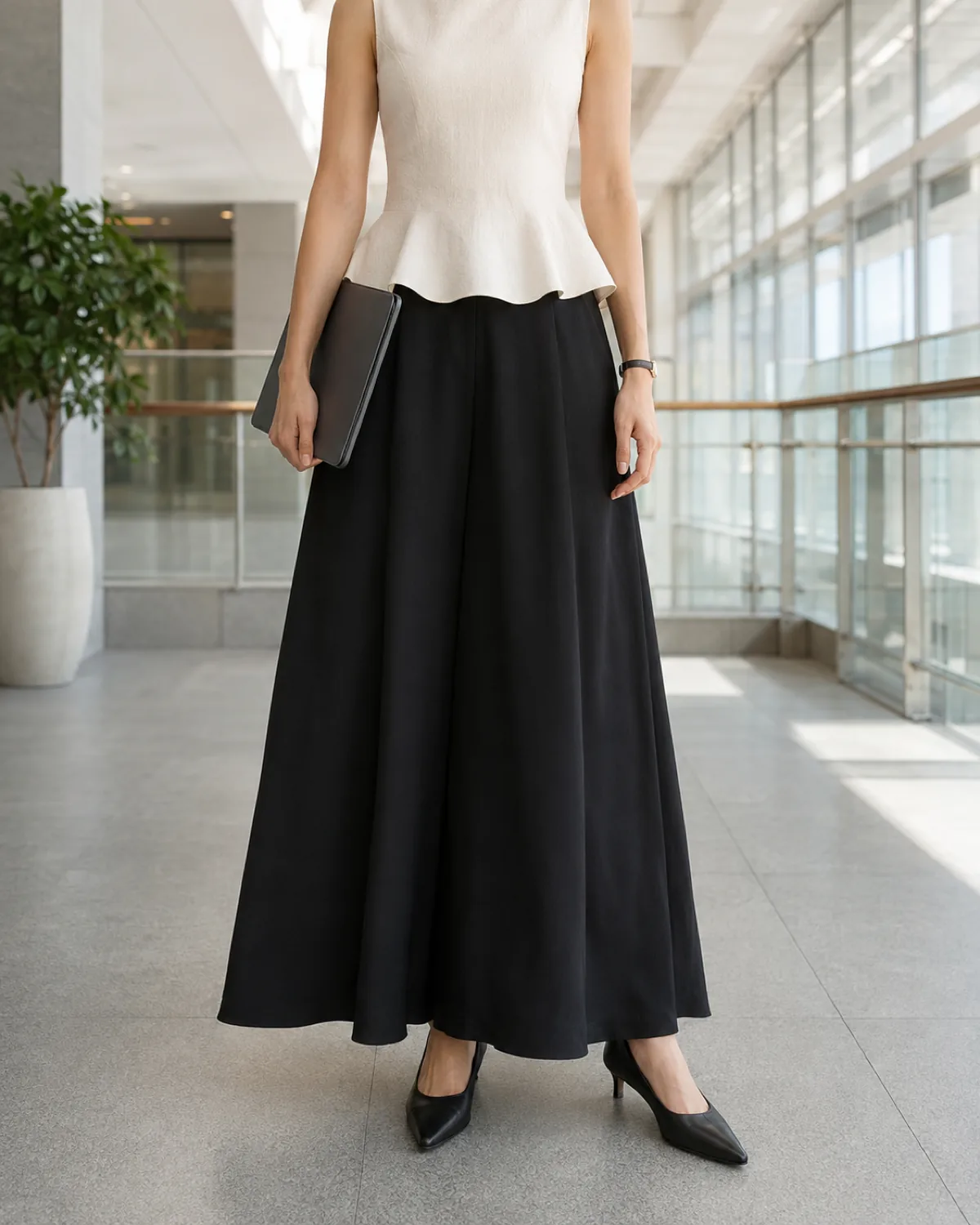 A woman in black palazzo trousers and an ivory peplum top, standing in a modern office atrium