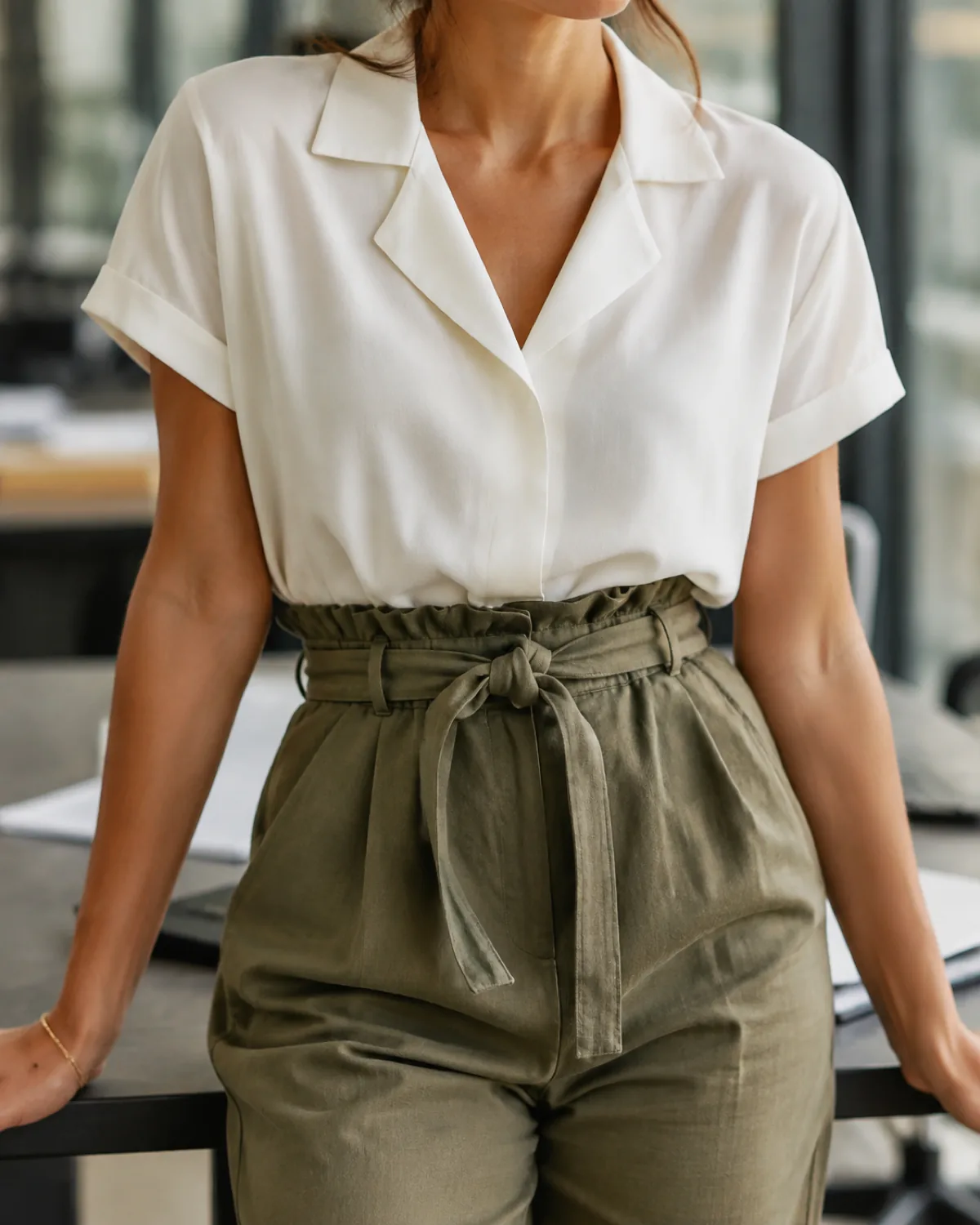 Close crop showing olive paper-bag waist trousers with a white camp-collar blouse French-tucked