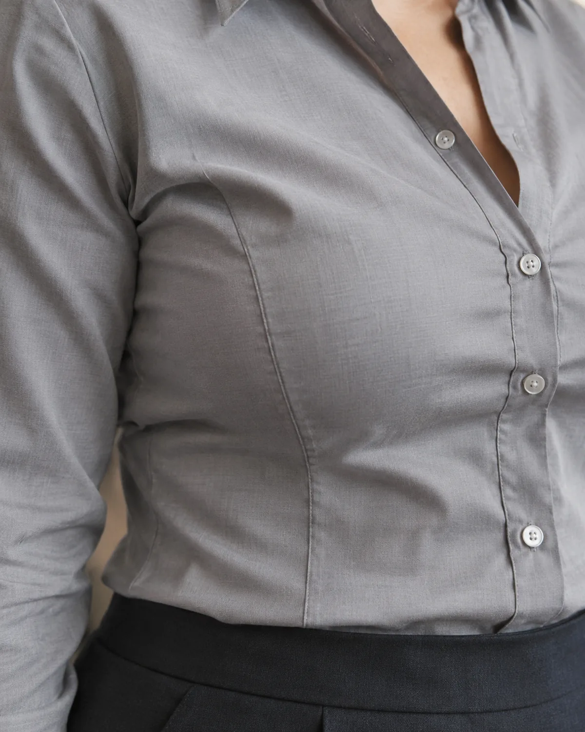Close crop on the torso of a grey structured cotton shirt showing a visible princess seam running vertically from under the bust toward the waist, shaping the fabric smoothly