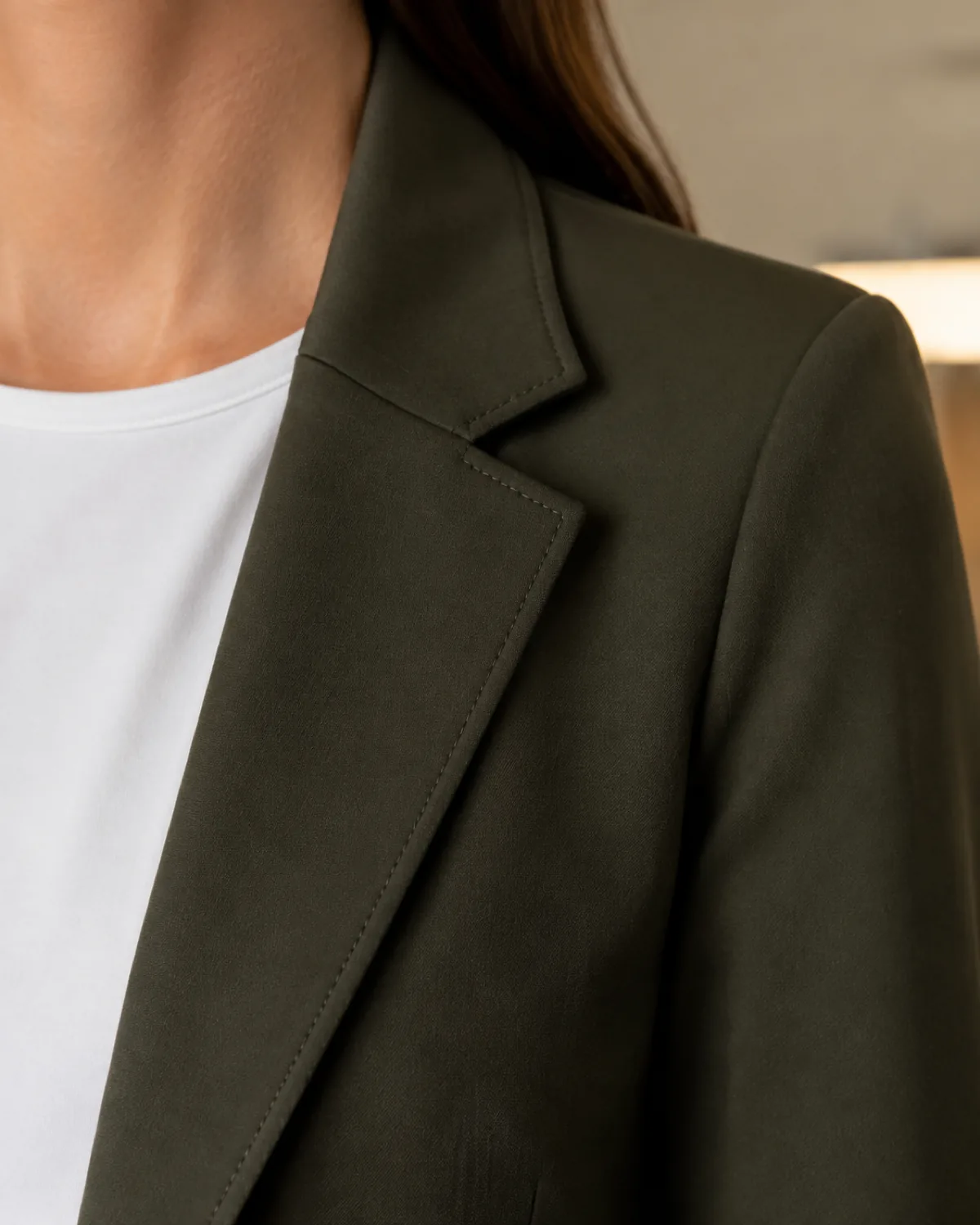 Close crop from collar to mid-chest of a woman wearing a dark olive ponte blazer with visible lapel stitching over a round-neck white tee