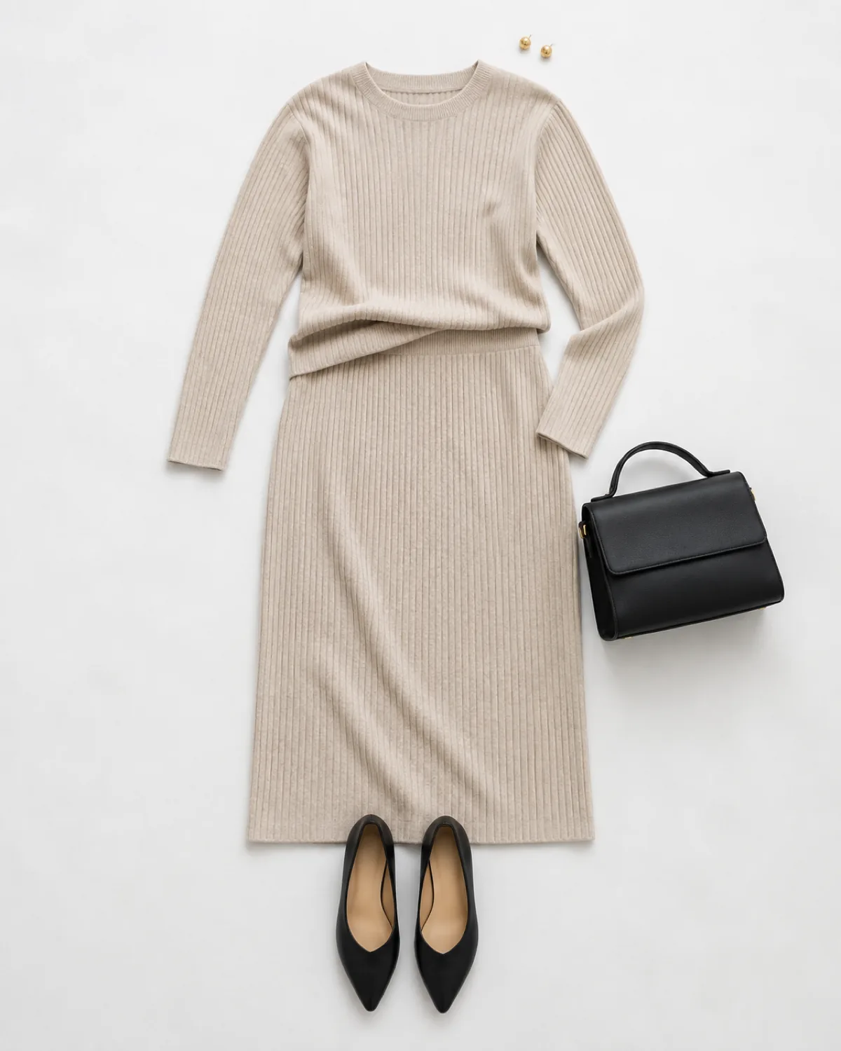 Overhead flat-lay of an oatmeal ribbed knit midi skirt and matching crewneck top with black pointed-toe flats, a structured black bag, and gold stud earrings